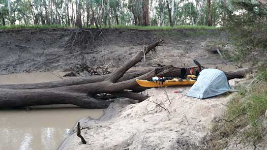 Tent on small beach beside large log in the river