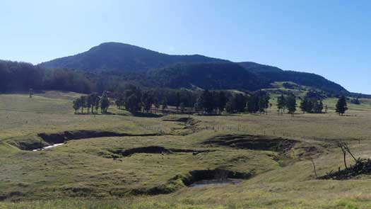 Looking over farmland with a stream towards a large rounded and forested mountain