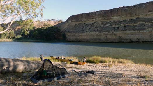 Tent on a beach beside a river and tall cliff