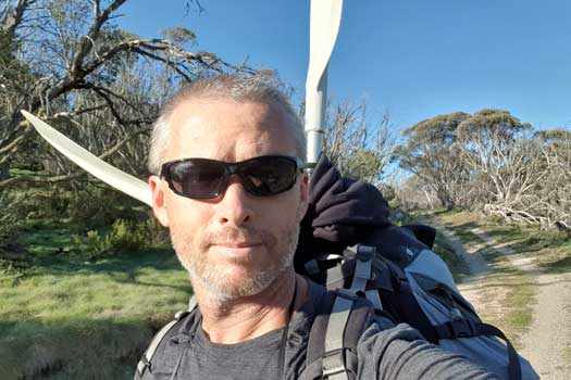 Author walking a firetrail carrying pack with paddles